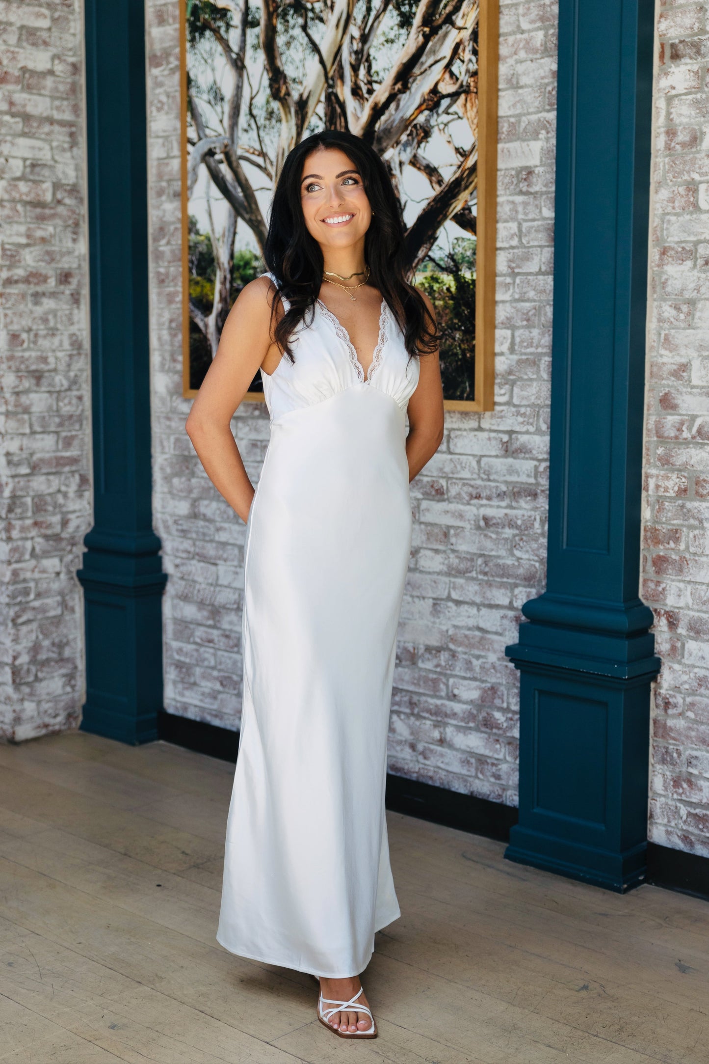Bride in a white bridal slip dress with lace details standing in front of a brick wall with a painting
