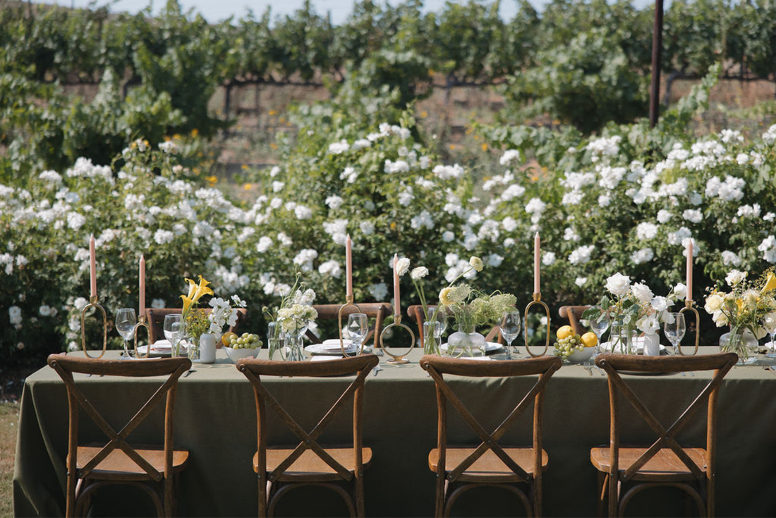 A gorgeous table setting with yellow flowers, candles, and rustic wooden chairs.