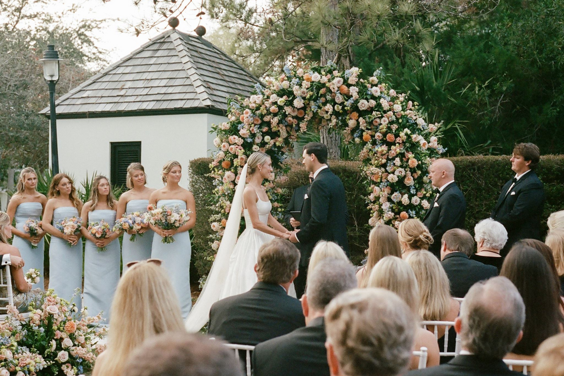 Perra and Ryan's elegant outdoor wedding ceremony at Rosemary Beach, Florida, featuring a romantic floral arch, pastel bridesmaid dresses, and classic coastal wedding style