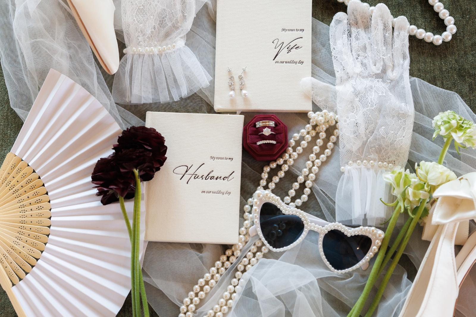 Flatlay photo of wedding accessories that include lace gloves, flowers, vow books, shoes, and veil