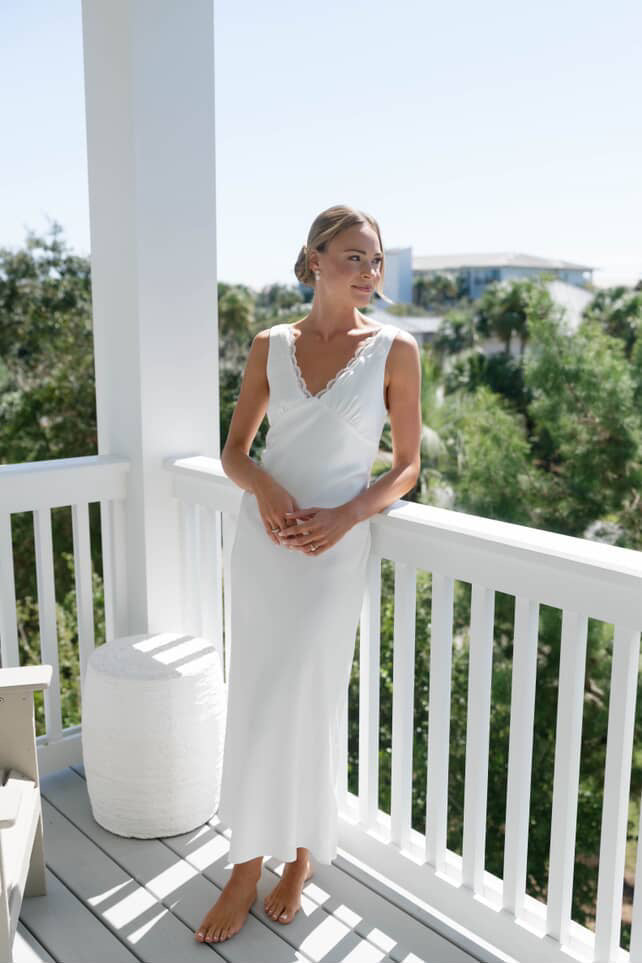 Bride in a white slip dress dress standing on a balcony with greenery in the background