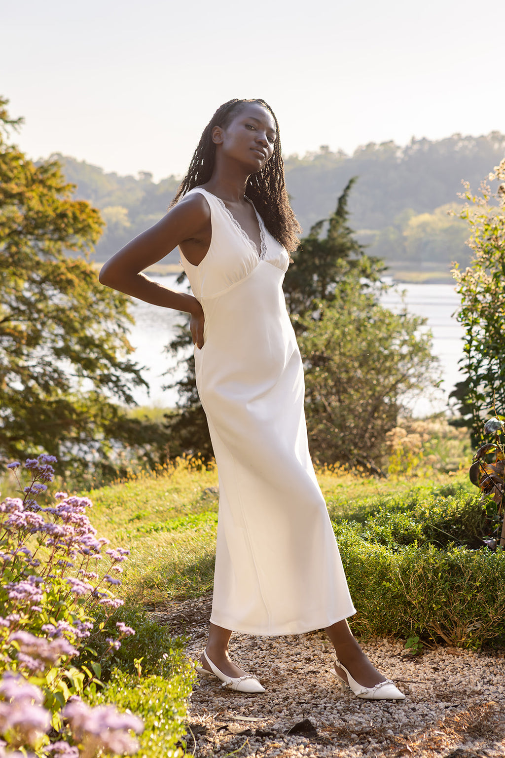 Bride in a white dress standing in a natural setting with trees and water in the background