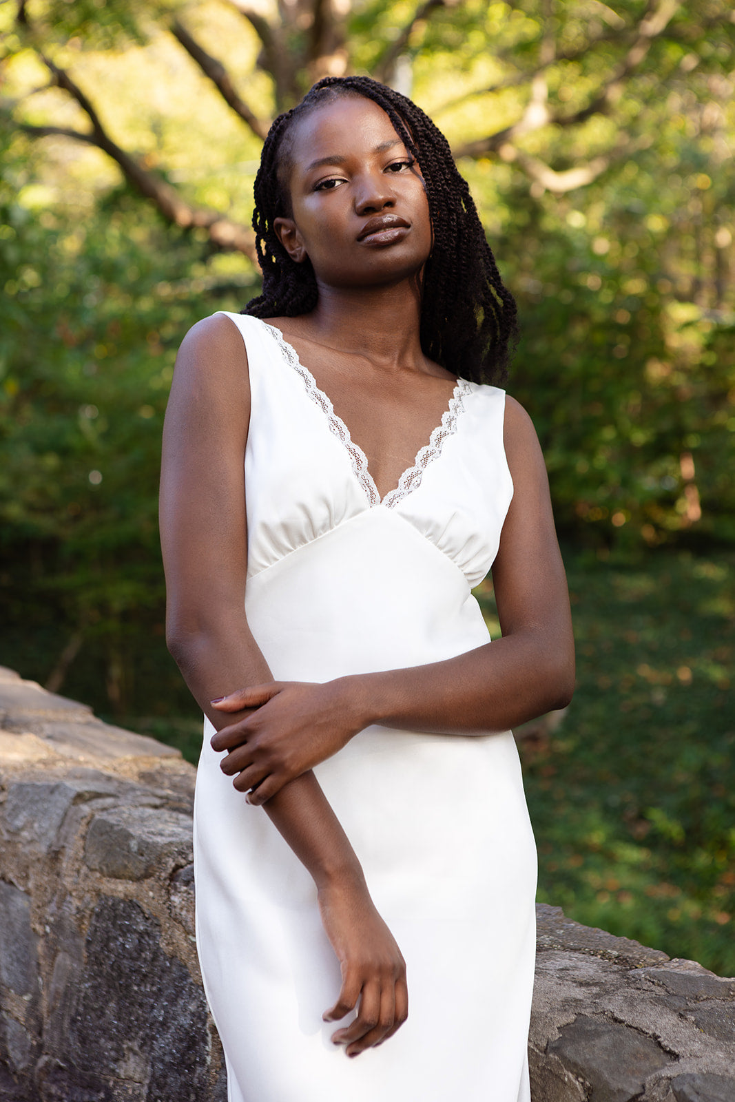 Model in a white slip dress standing outdoors with greenery in the background