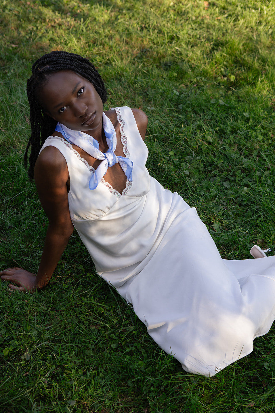 Woman in a white slip dress with a blue silk scarf sitting on grass