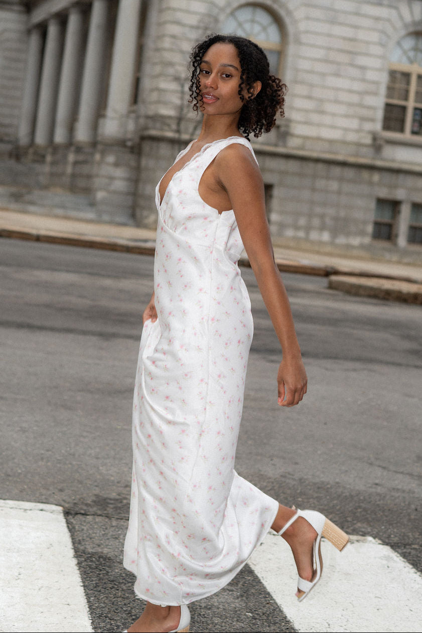 Woman in a white floral dress walking on a street with a large building in the background