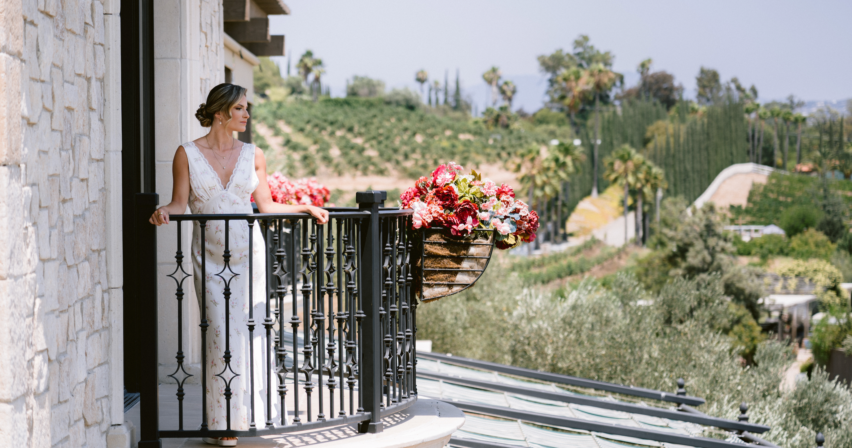 Bride in a floral slip dress standing on a balcony with a scenic background