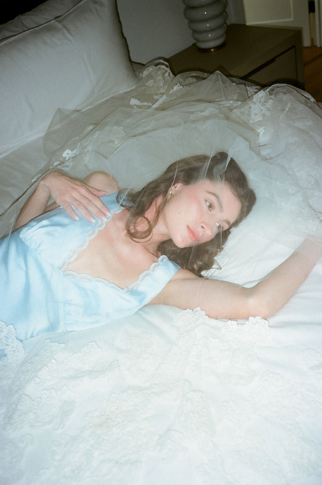 Woman in a light blue slip dress lying on a white bedspread