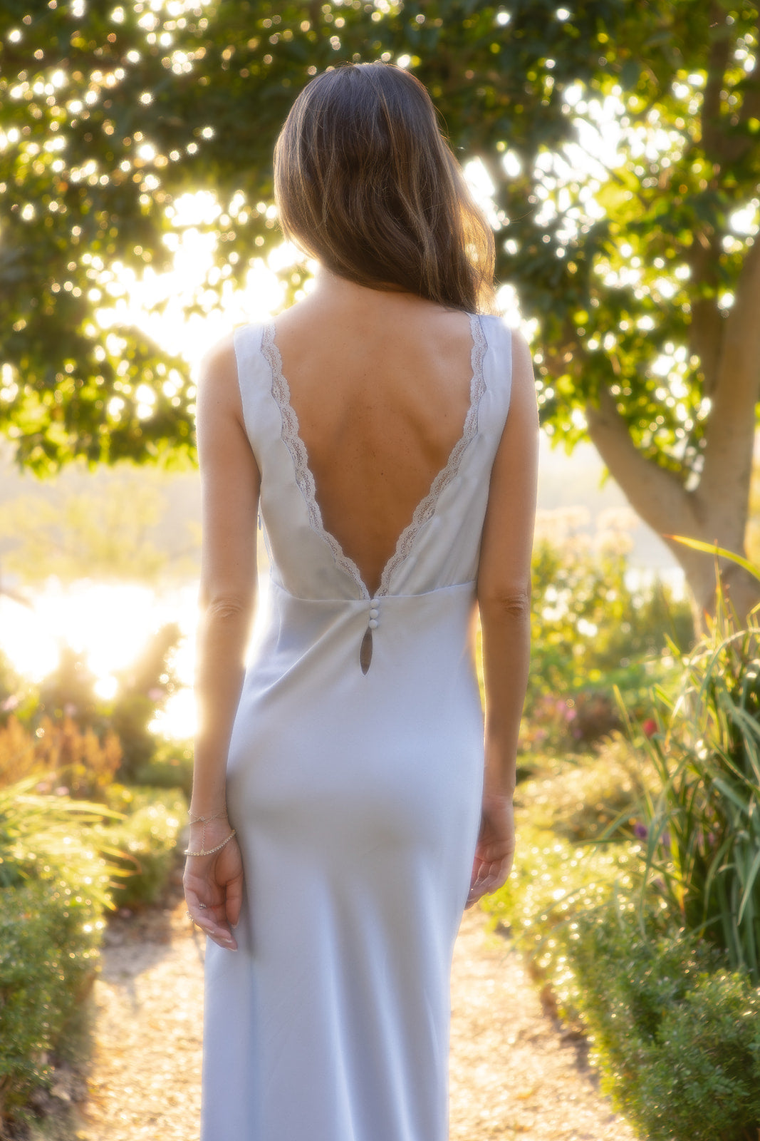 Bride in the something blue slip dress with an open back standing in a garden