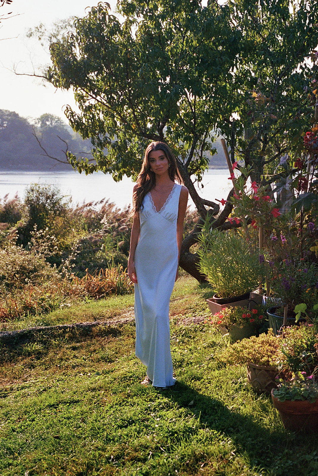 Model in the something blue slip dress with lace details standing in a garden with beautiful flowers