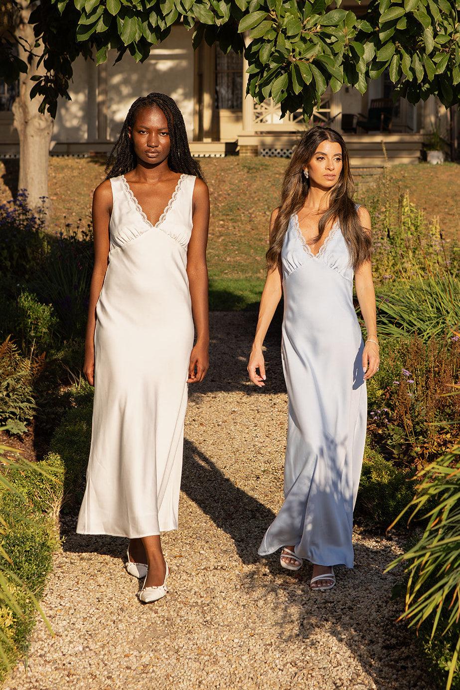 Two models wearing bridal slip dresses with lace details walking through a garden