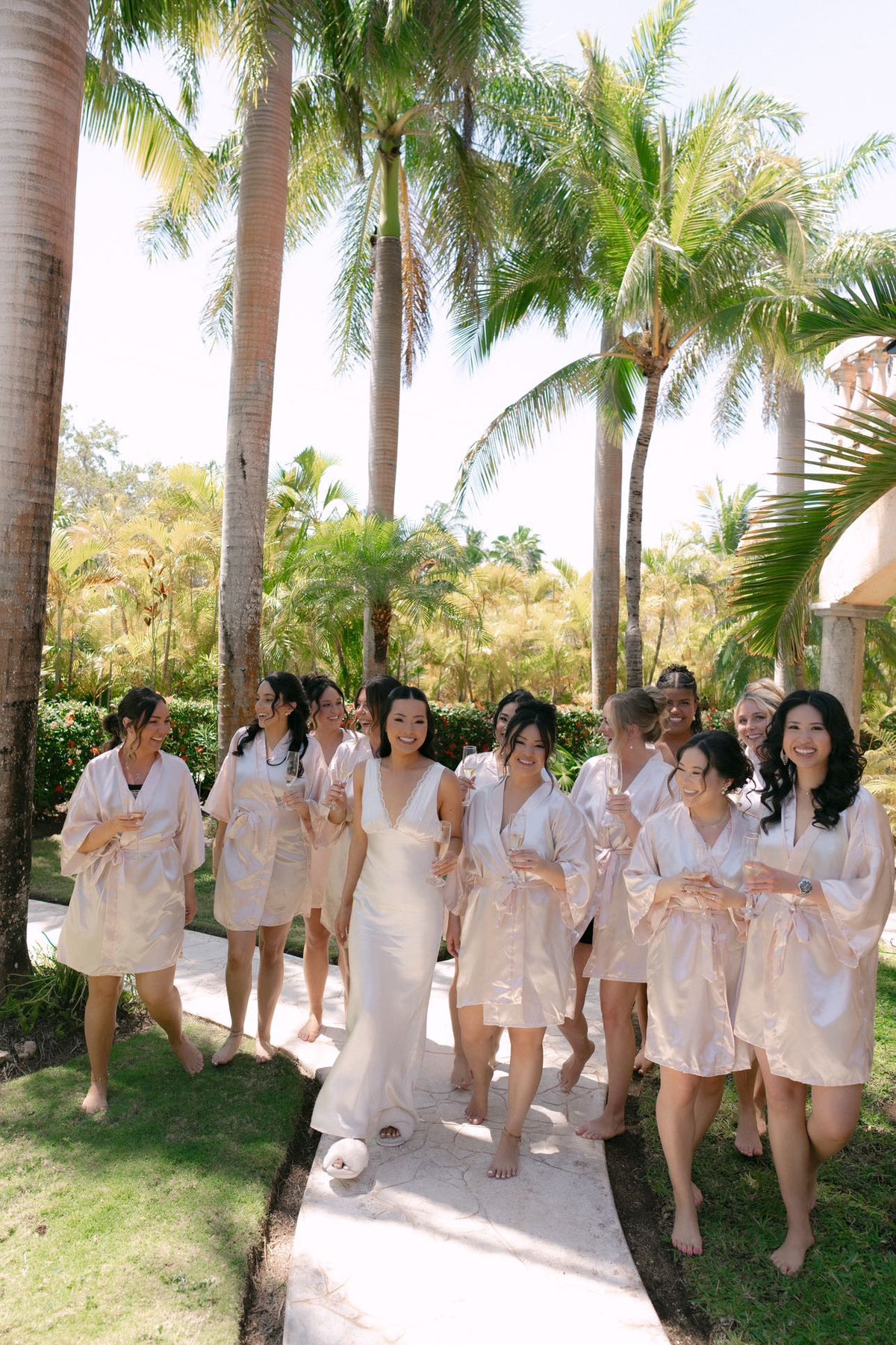 Bride in a white slip dress outside with her bridesmaids in champagne robes
