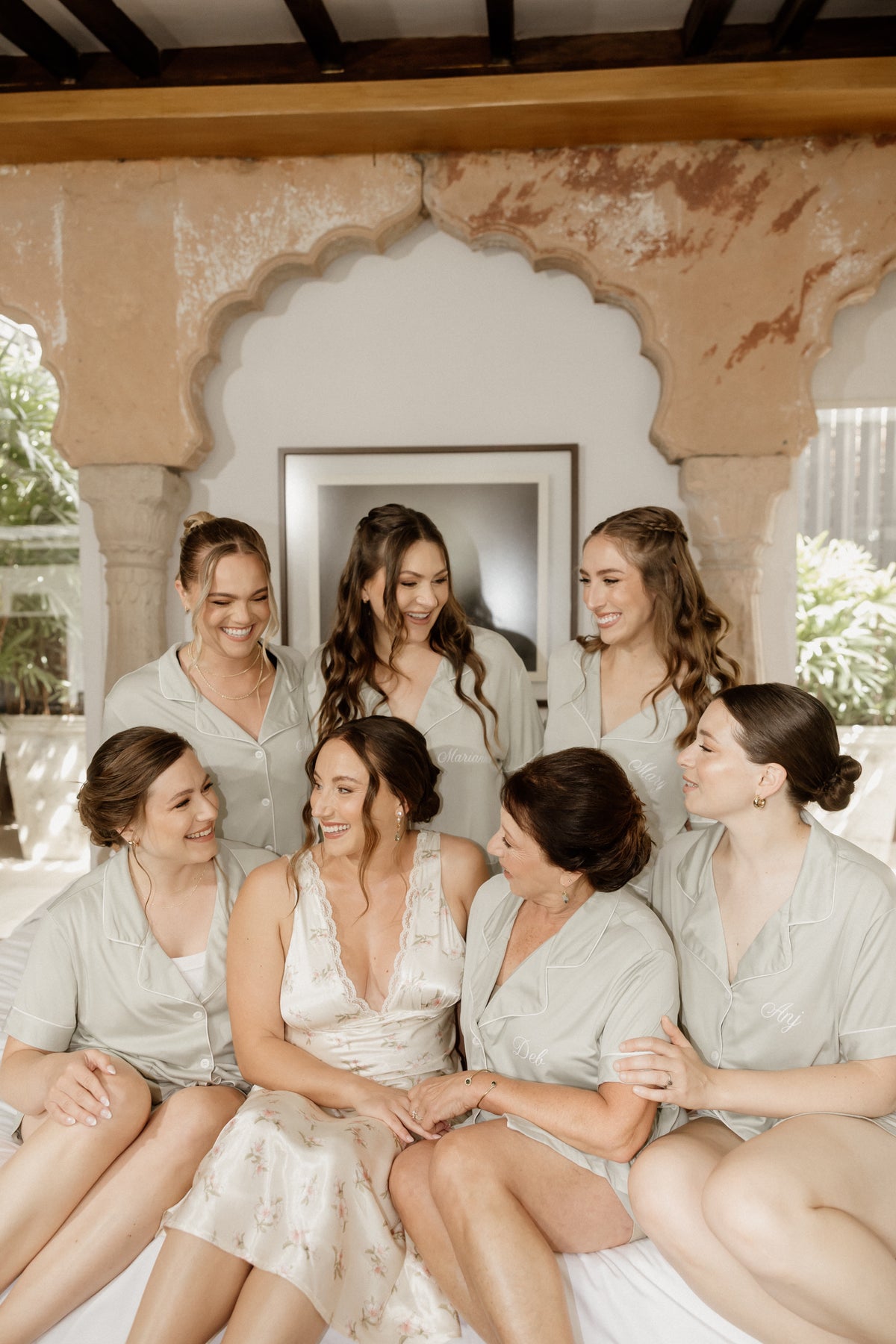 Bride wearing a floral slip dress the morning of her wedding day sitting with her bridesmaids in matching pjs
