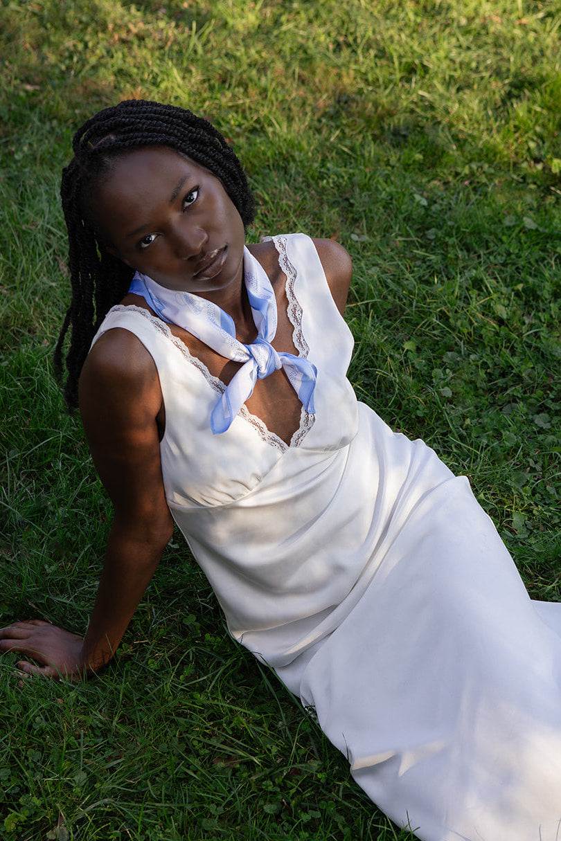 Woman in a white slip dress with a blue silk scarf sitting on grass